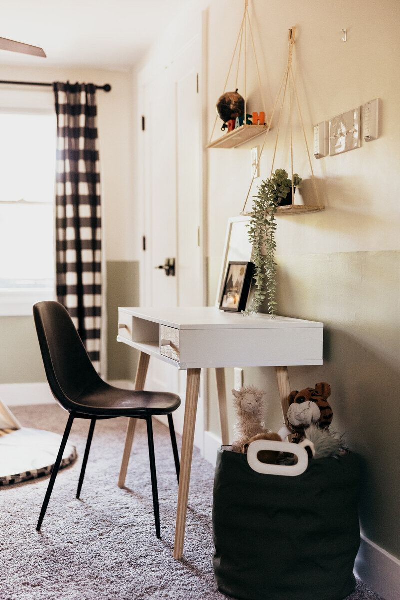 A colorful interior design featuring a child's desk and chair, hanging shelfs and a bin of stuffed animals. 