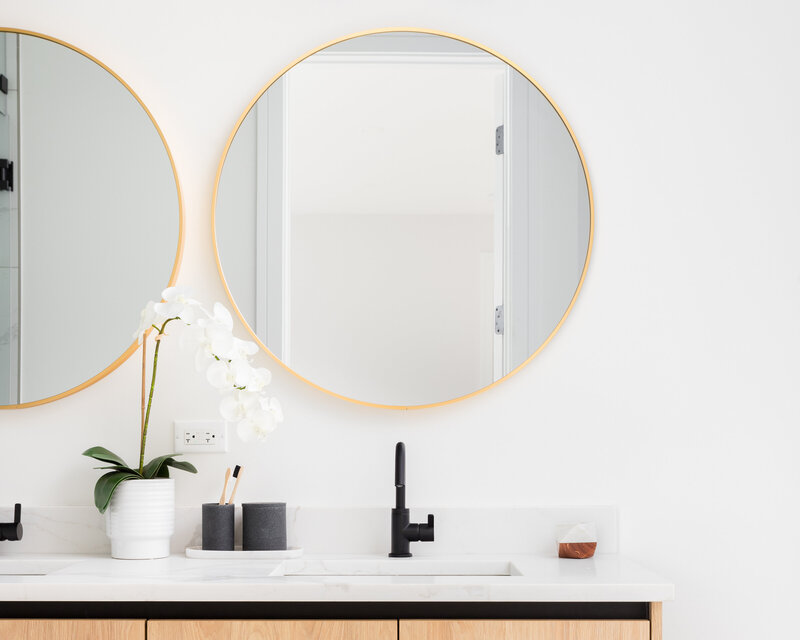 Modern farmhouse bathroom design with a double vanity and gold circle mirrors.