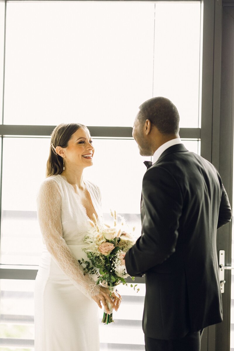 A bride and groom are smiling at each other during their first look standing on a New York City balcony.