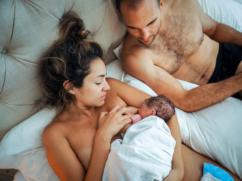 Woman and man lying on a bed holding a newborn baby