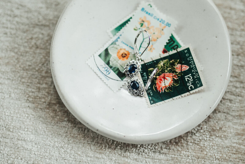 a collection of stamps and a pair of earrings in a small white dish