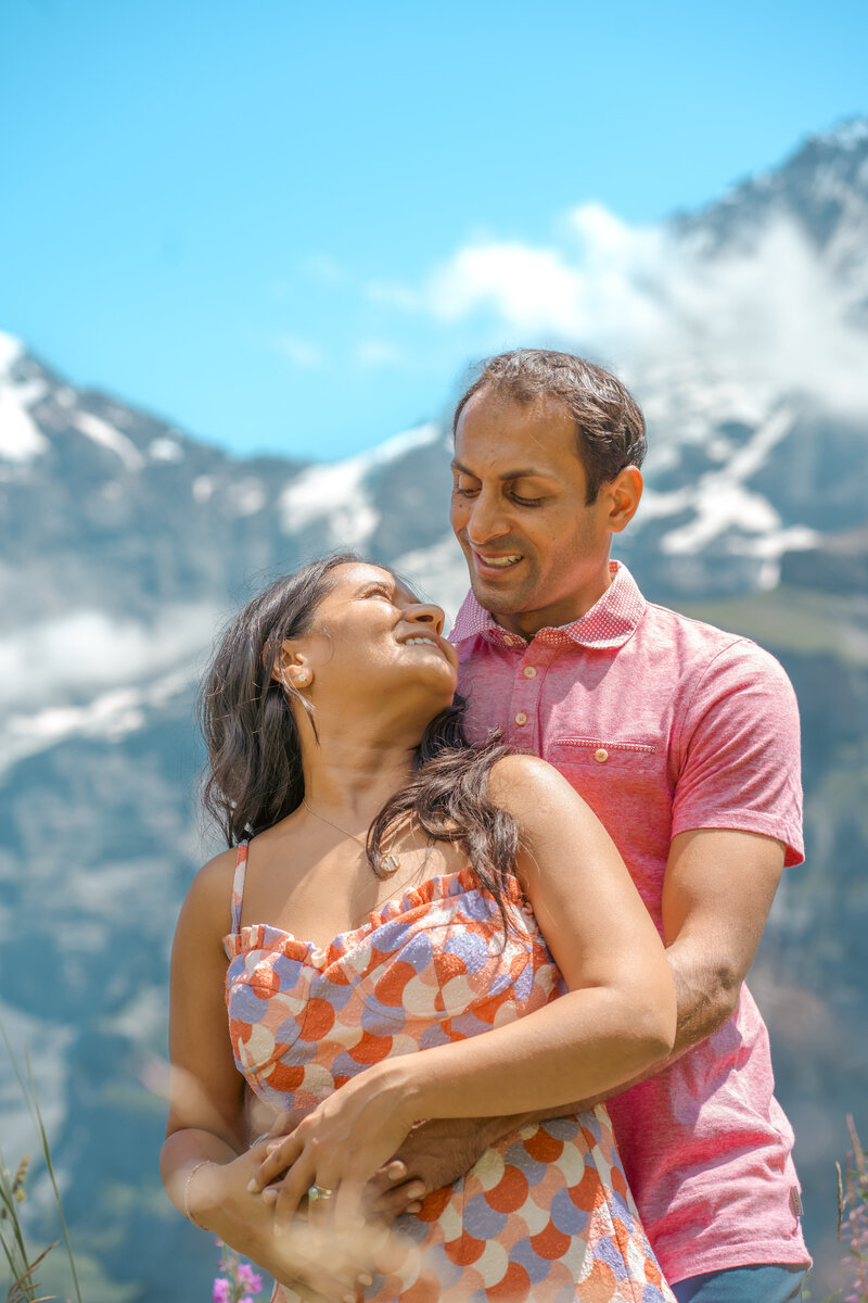 Ein verliebtes Paar blickt sich tief in die Augen, während sie die majestätische Kulisse von Lauterbrunnen, Schweiz, im Hintergrund genießen. Eine Liebe, die von der Schönheit der Natur umrahmt wird.