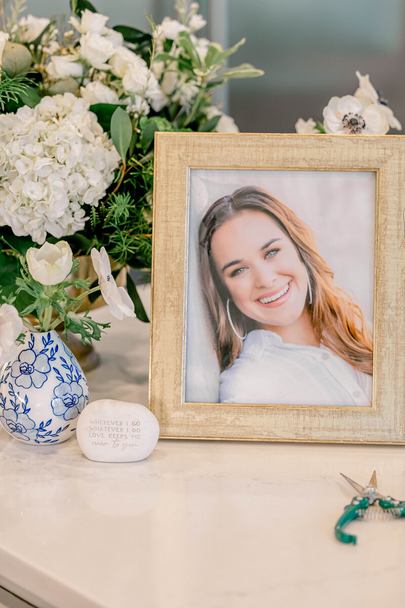 Dark haired girl in picture frame sitting on counter next to a vase of flowers