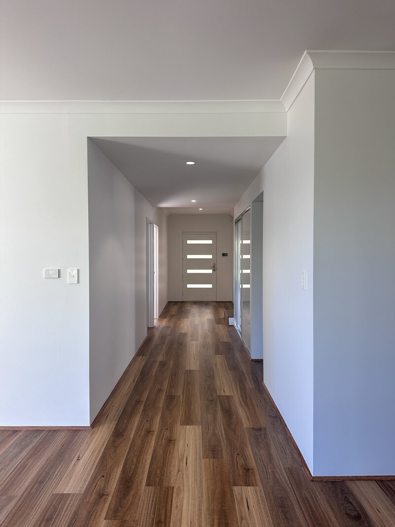 Hallway has wooden floors, entrance door at the end and Casper white walls