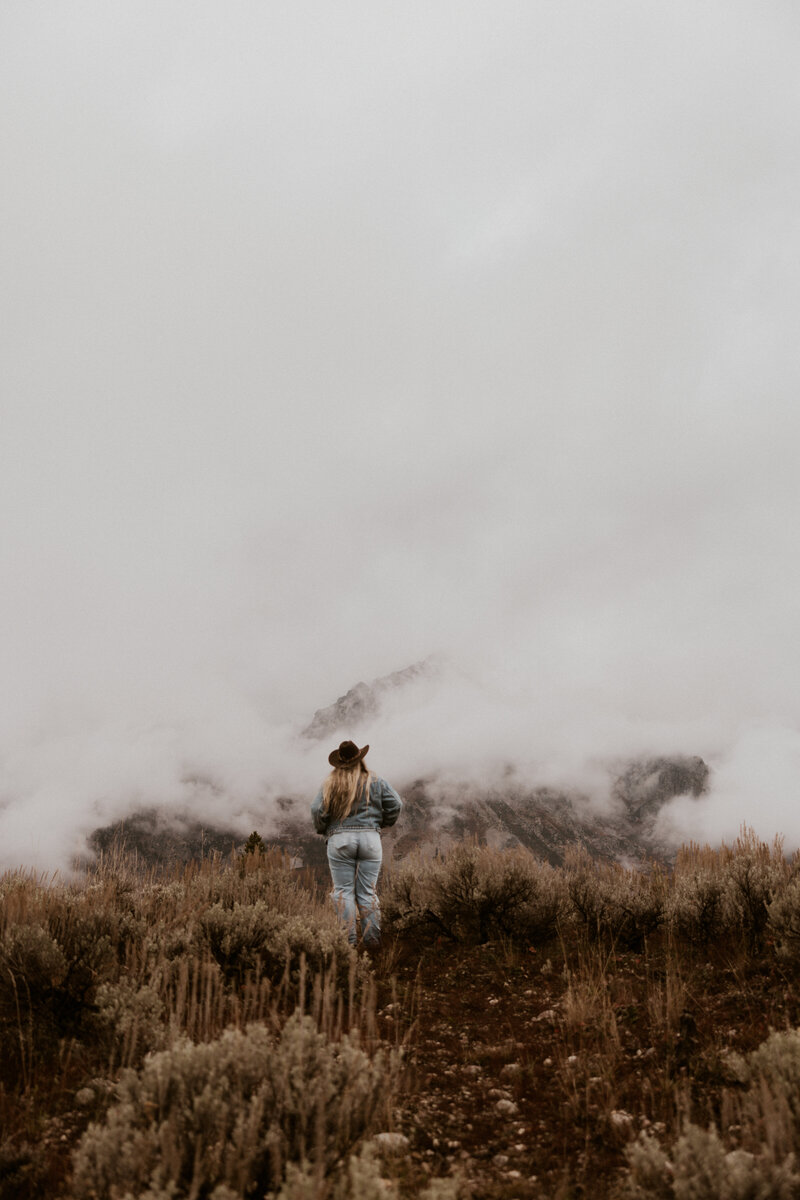 woman standing in front of mountains and holding her hair