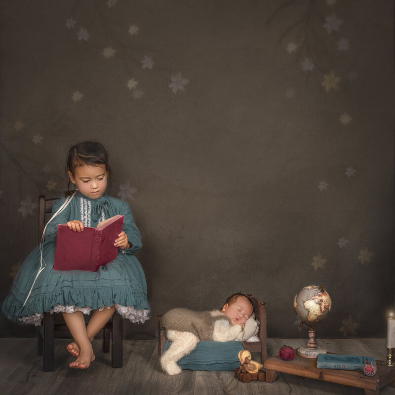 big sister reading a storybook to their newborn sibling, capturing a heartwarming family moment in a fine art photography session in Ottawa."