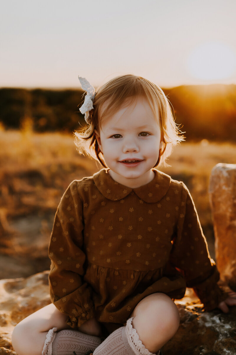 A young girl in a polka dot romper sitting on a boulder in Decatur, TX