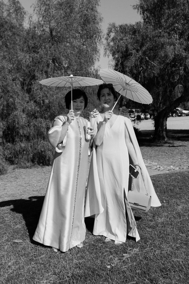2 wedding guests pose for portrait while holding sun parasols