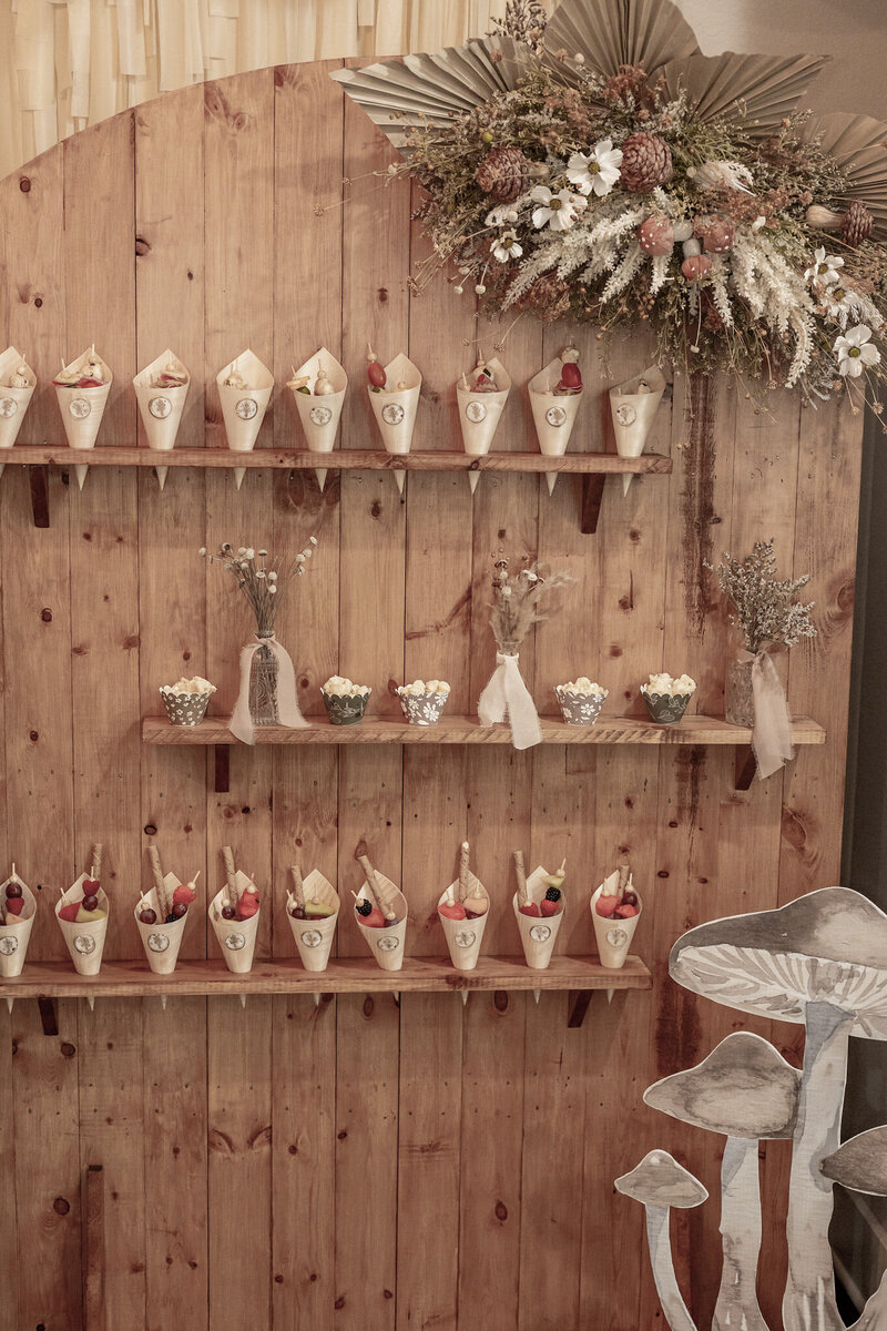 Wood arch with shelves holding charcuterie cones and flower vases. 