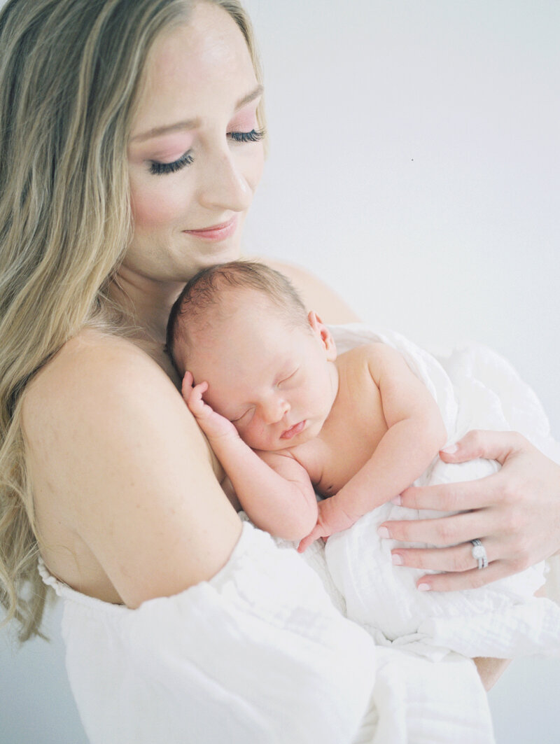 Blonde mother holds newborn up to her chest photographed by Newborn Photographer Maryland Marie Elizabeth Photography