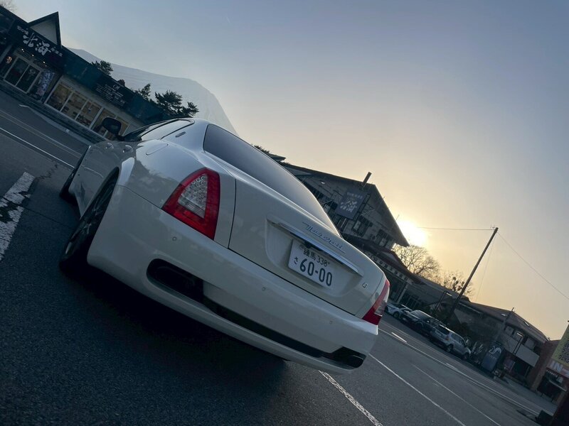 Rear view of a white Maserati Quattroporte, parked under a golden sunset sky, capturing the refined luxury and distinctive tail light design of the vehicle.