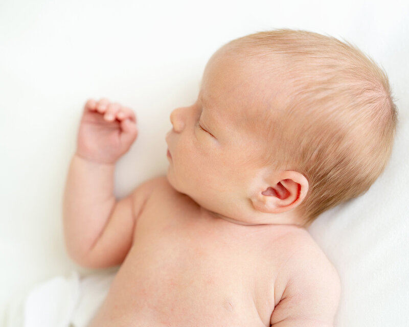 Six month old baby boy wearing white knit romper laughs at family photographer Julie Brock at her Louisville KY photography studio