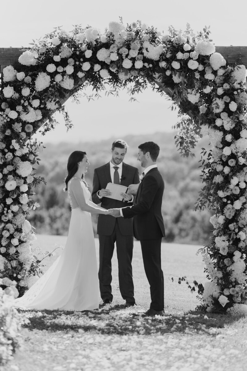 Wedding couple stands under large floral arch by clayton floral at Maquam barn and winery with lindsey leichthammer events