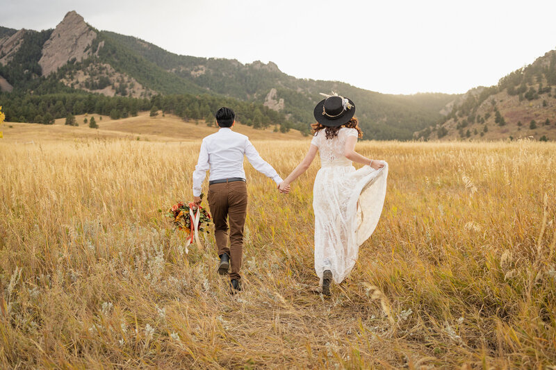 A couple runs through a meadow with mountain views during their elopement