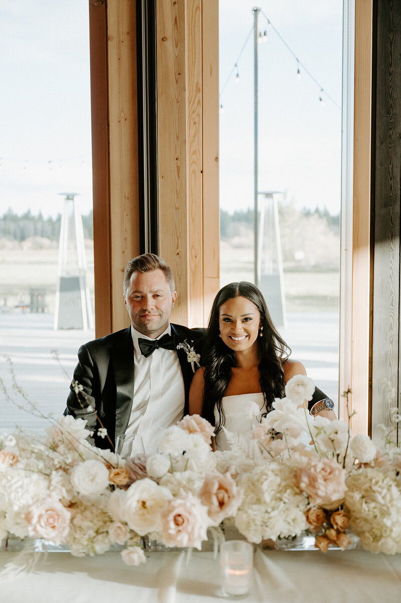 Close-up of reception table with white hydrangea, neutral roses, and bleached fern in lucite vases, styled with candlelight at Jenay and Daniel’s wedding by Summer Robbins Flowers in Central Oregon