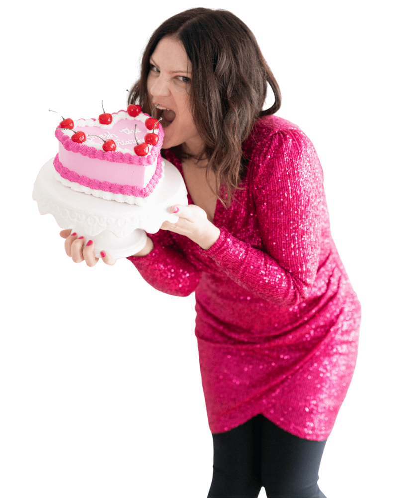 Emily, brand strategist, wearing a pink dress, taking a bite of a pink heart shaped cake that says "smash the patriarchy."