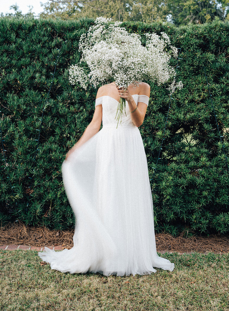 A playful bridal moment in New Orleans, with the bride holding her bouquet in front of her face and the skirt of her gown, epitomizing fine art wedding photography.