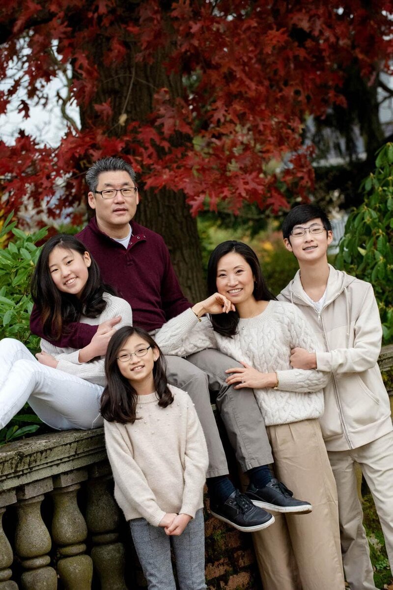 Happy father and color coordinating mother and her 2 daughters and son, at the park with fall trees.