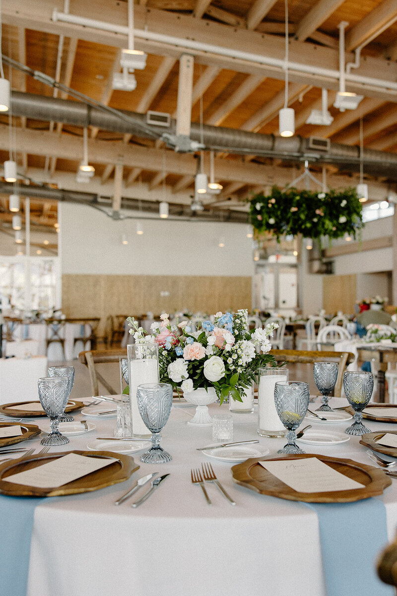 Elegant waterfront reception tablescape with blush florals, crystal glassware, and dusty blue chargers