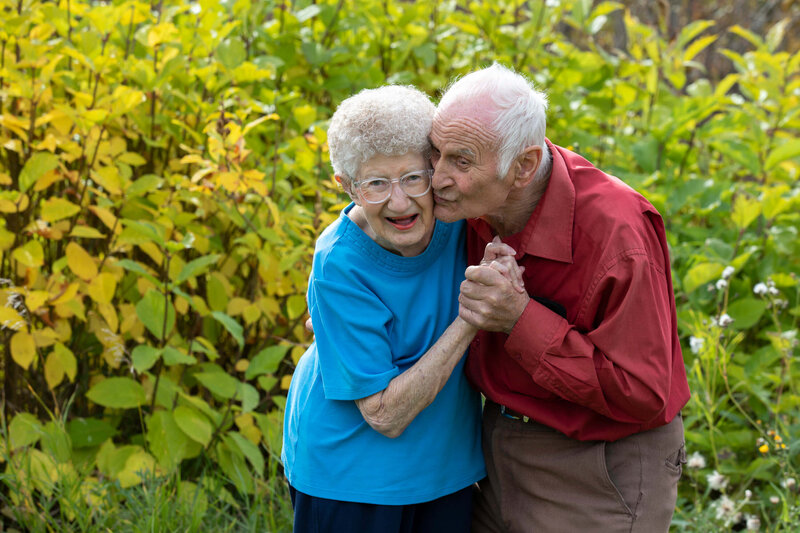 elderly couple lovingly embraces as husband kisses wifes cheek