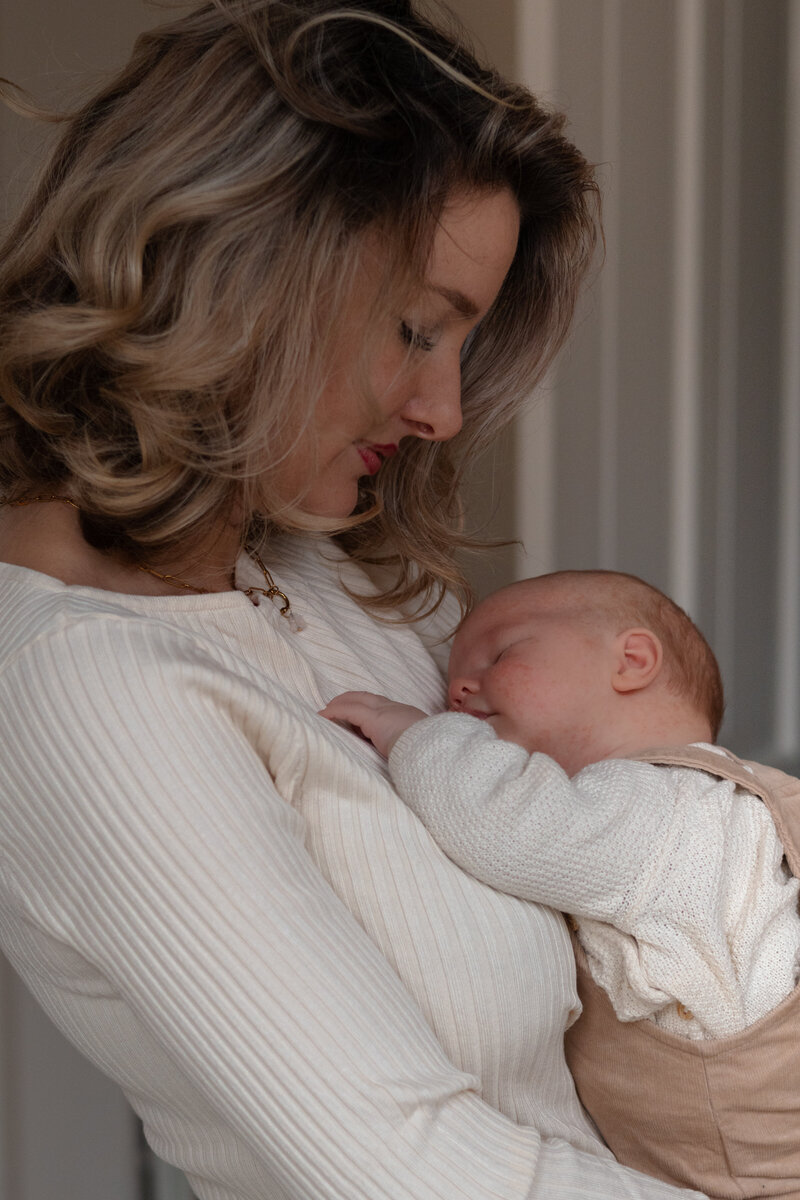 Een vrouw houdt een baby vast, met een liefdevolle blik en een warme omhelzing.