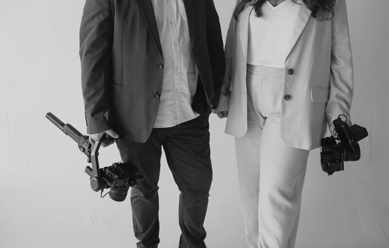 Black-and-white portrait of Tyler and Makenzie, wedding videographers from Jacksonville, holding their cameras and ready to film a wedding