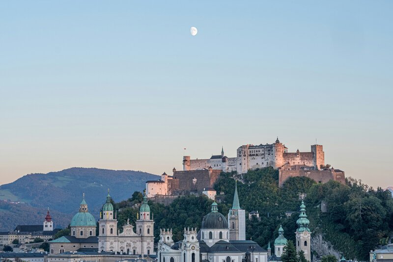 Eine Gruppe von Menschen nimmt an einer geführten Nachtwächter-Tour durch die historischen Gassen von Salzburg teil. Der Nachtwächter trägt traditionelle Kleidung und hält eine Laterne, während er spannende Geschichten erzählt.