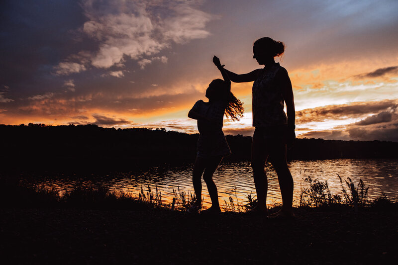 A mom spins her young daughter around at sunset while on vacation.