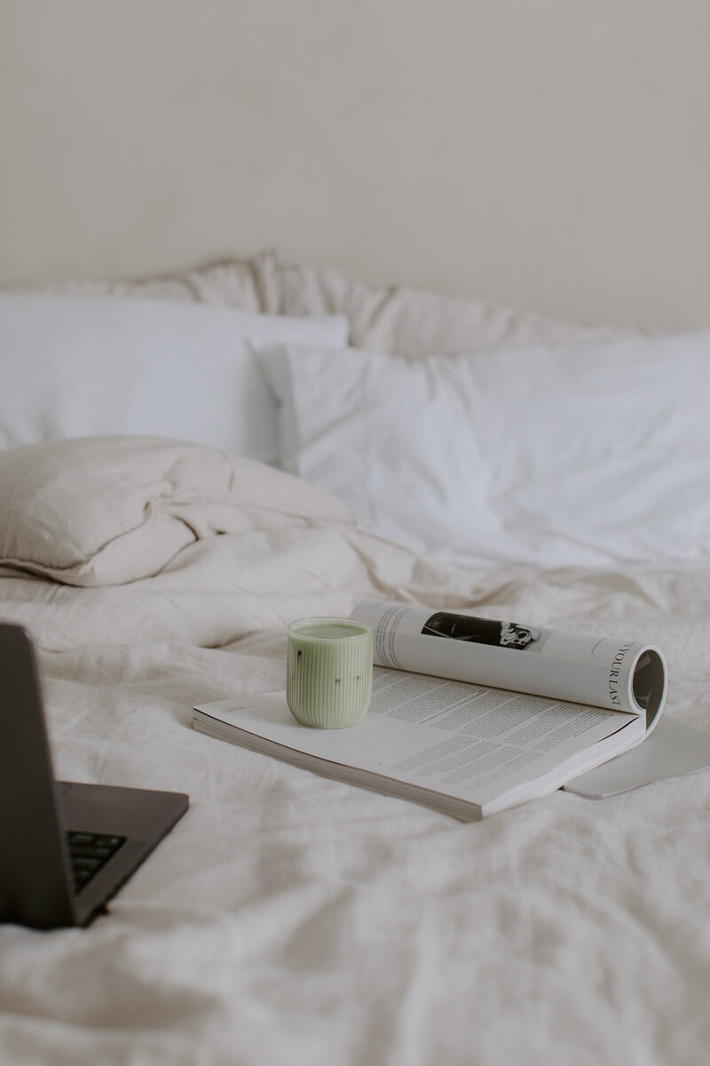 light colored bed with laptop and magazine with matcha