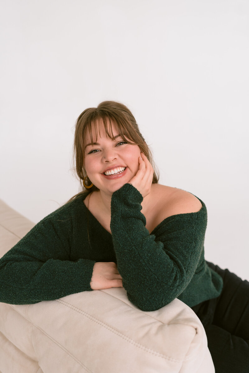 woman sitting against a couch smiling with one hand rested under her chin