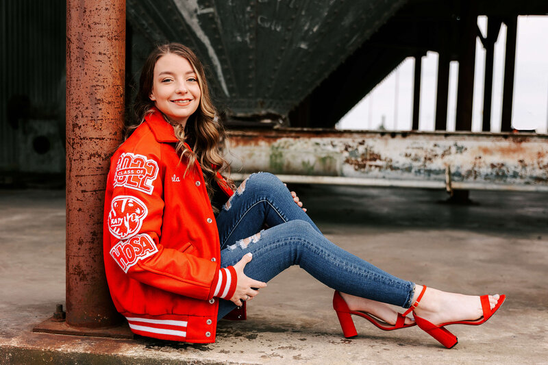 Girl in letterman jacket leaning on rusted post