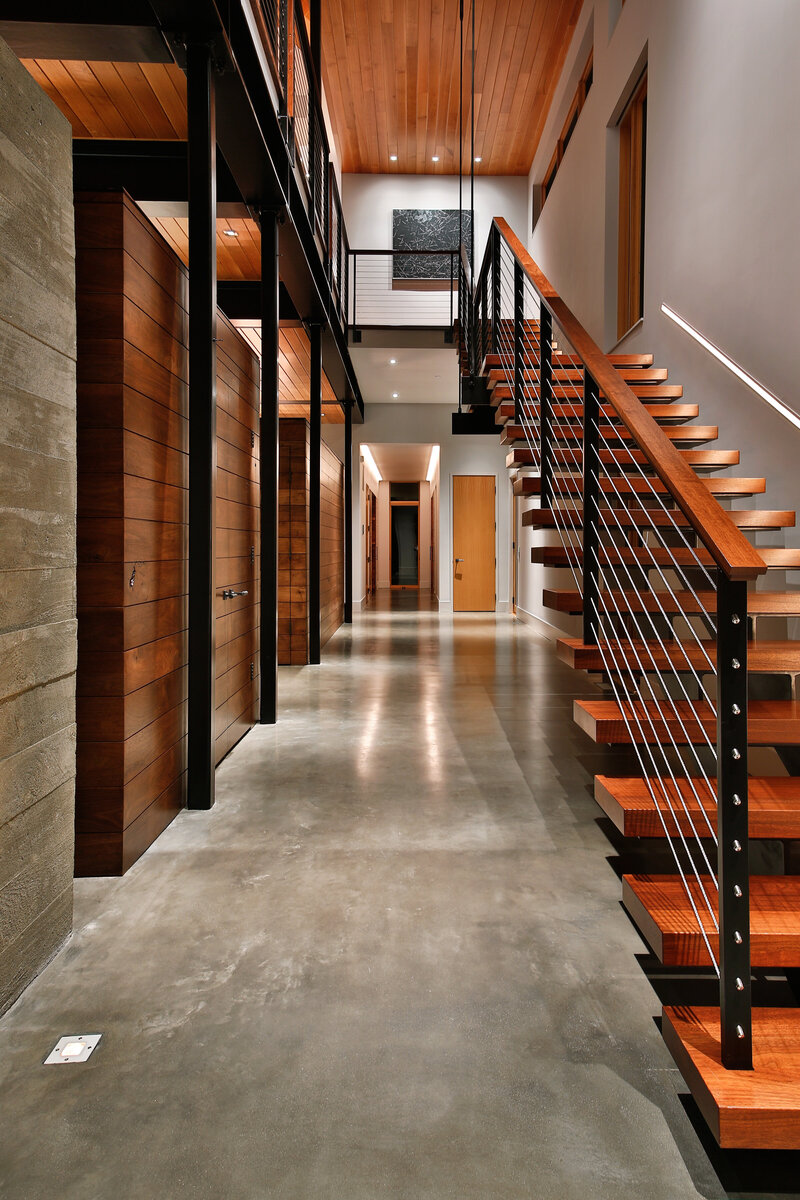 concrete hallway with dark wood accents and large staircase