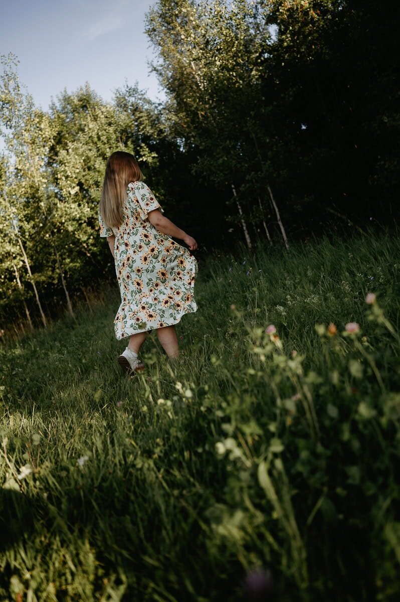 Gravid kvinna visar sin mage med att hålla upp klänningen och ler.