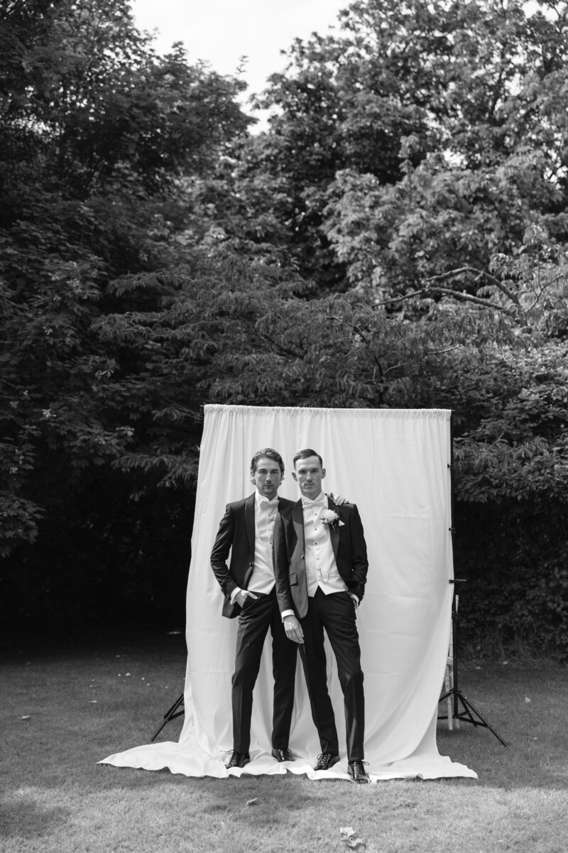 two grroms standing in front of white sheet backdrop