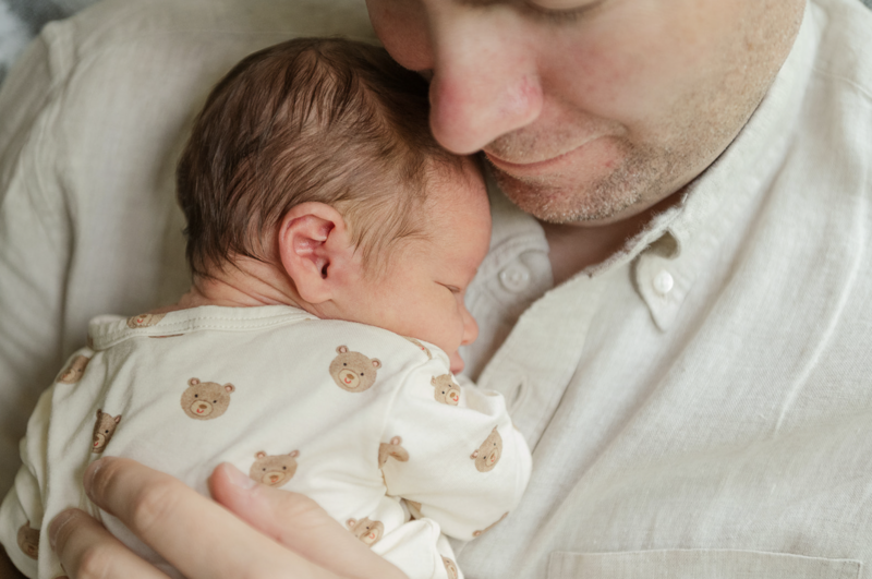 Father snuggling his newborn wearing a bear-print onesie during a lifestyle newborn session in Lancaster, PA.