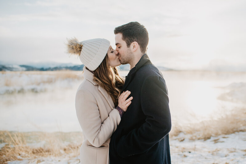 Grand Teton photos with man and woman kissing each other in front of a river that has rising fog at sunrise
