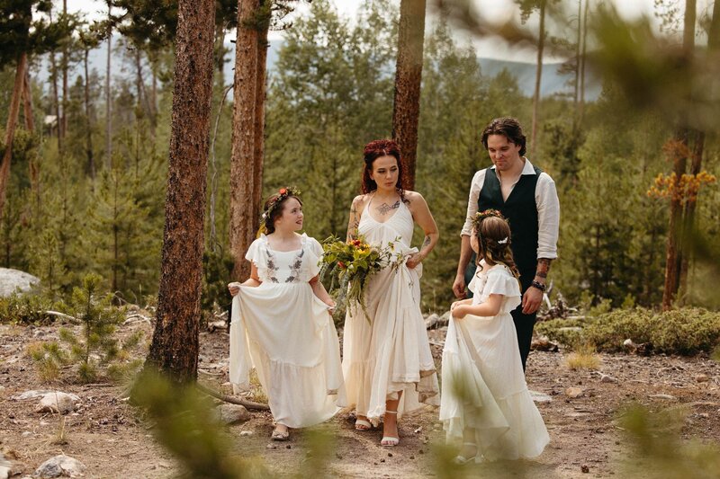 A bride and groom walk with their daughters through the forest