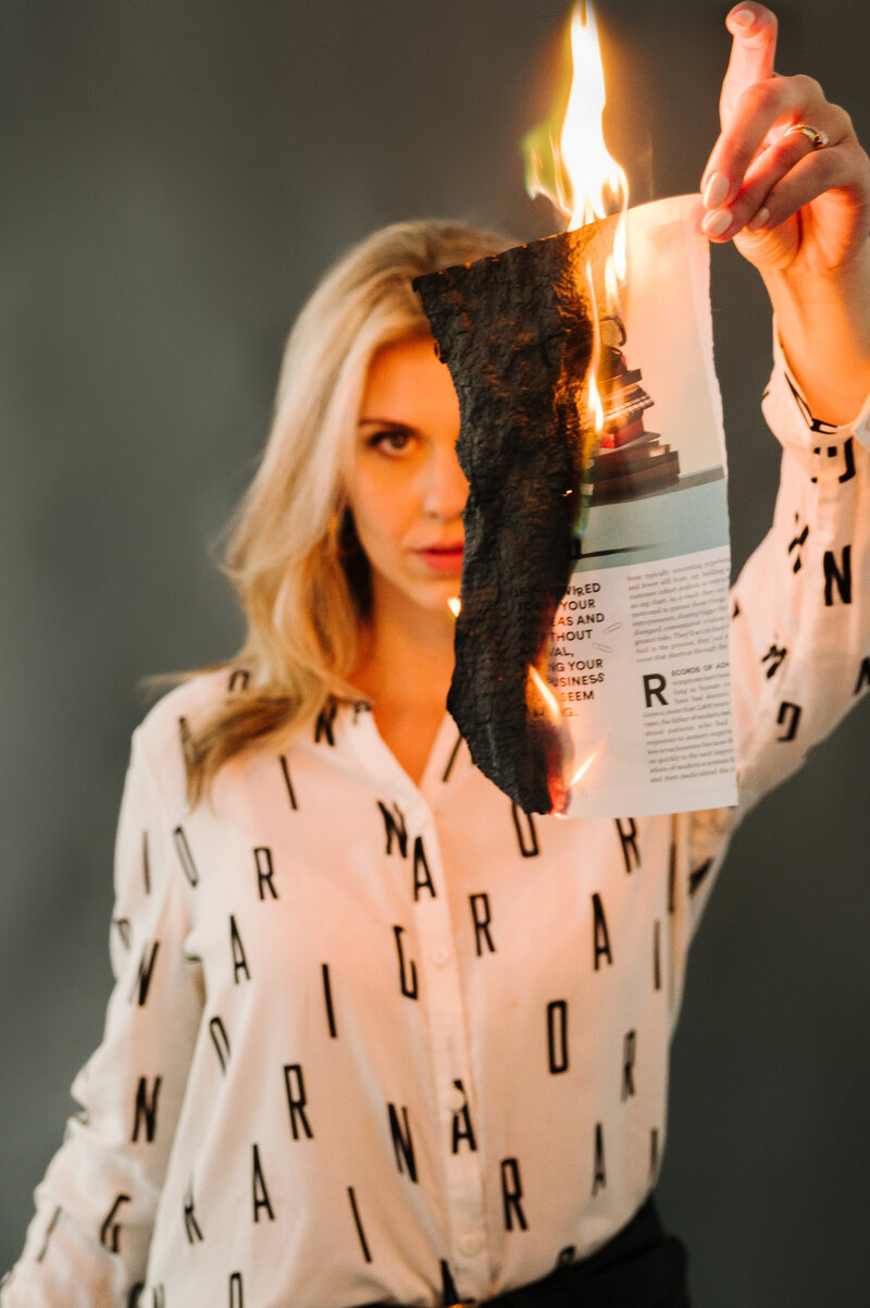 Sarah Klongerbo holding up a magazine page that she lit on fire