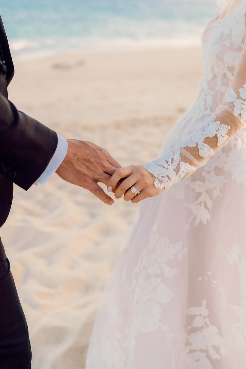 Close up photo of a bride and groom's joined hands on a beach