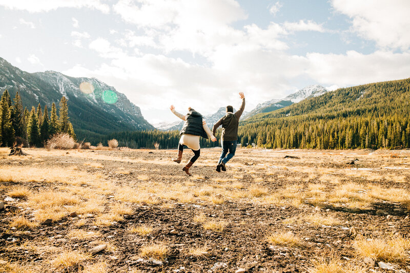Couple skipping through the field with mountain backdrop