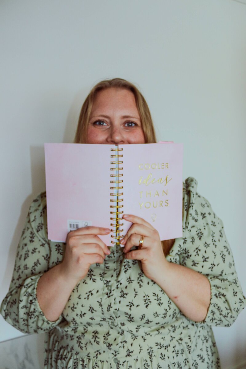 Stine Andersson smiling and peaking behind a planner as she plans blog manaagement for brand and web designers