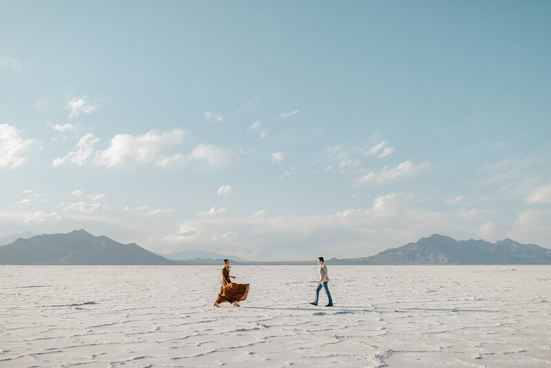 Couple walking barefoot across the Bonneville Salt Flats in Utah with mountains in the distance, captured during their adventurous couples session.