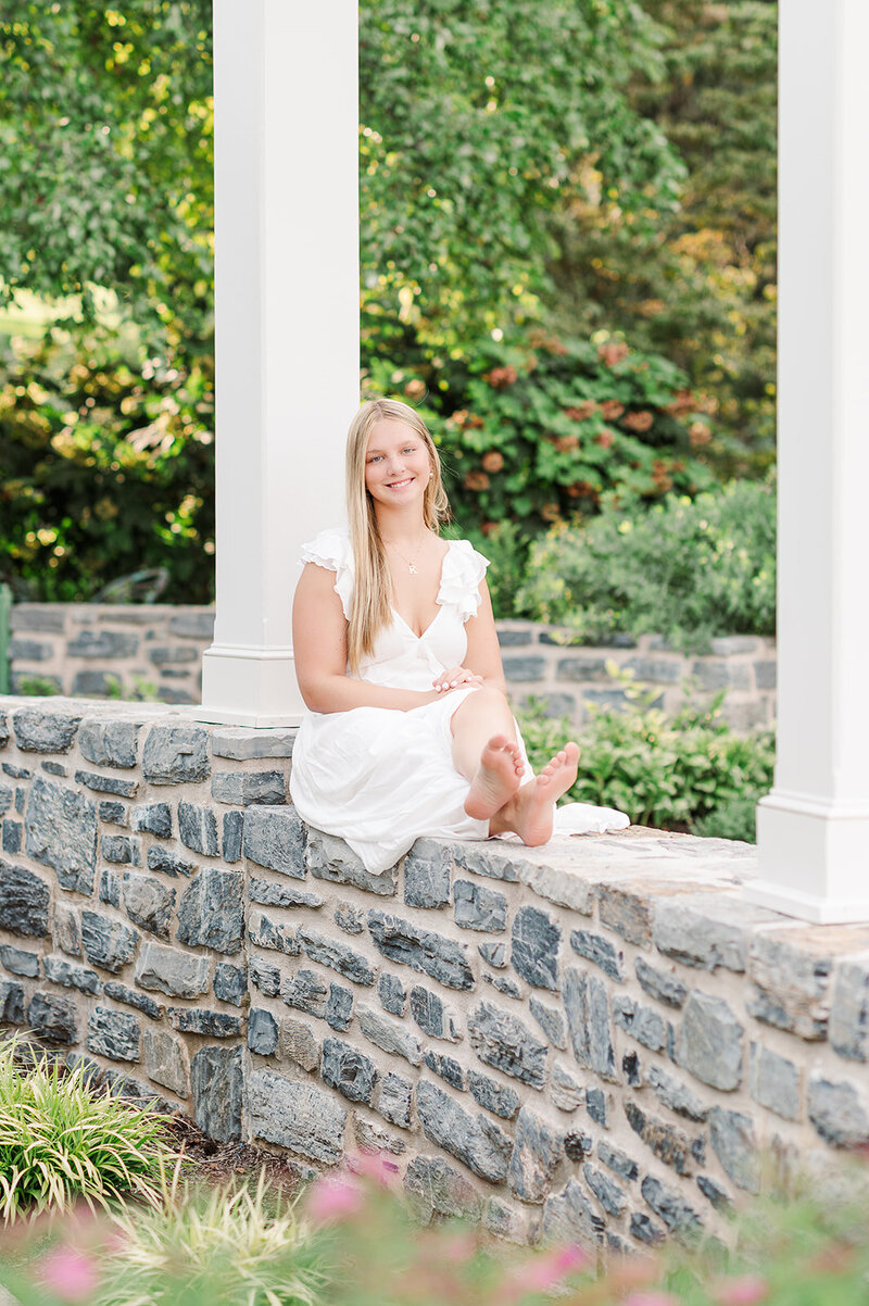 Senior girl sitting on a stone wall during session at hershey gardens