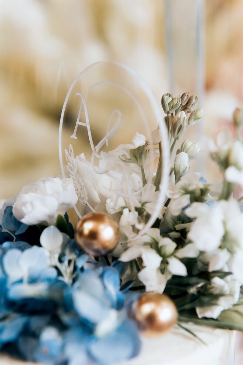 A wedding cake topper with blue flowers and rose gold balls.