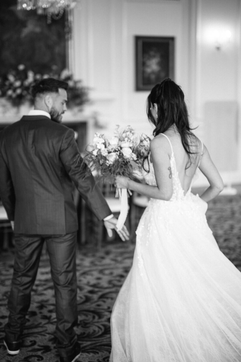 Black and white photo of the bride and groom walking side by side, seen from behind — a timeless and poetic moment captured with simplicity and grace