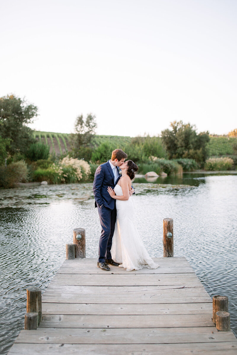 Bride and groom kiss at the end of a dock over water in Santa Ynez, California