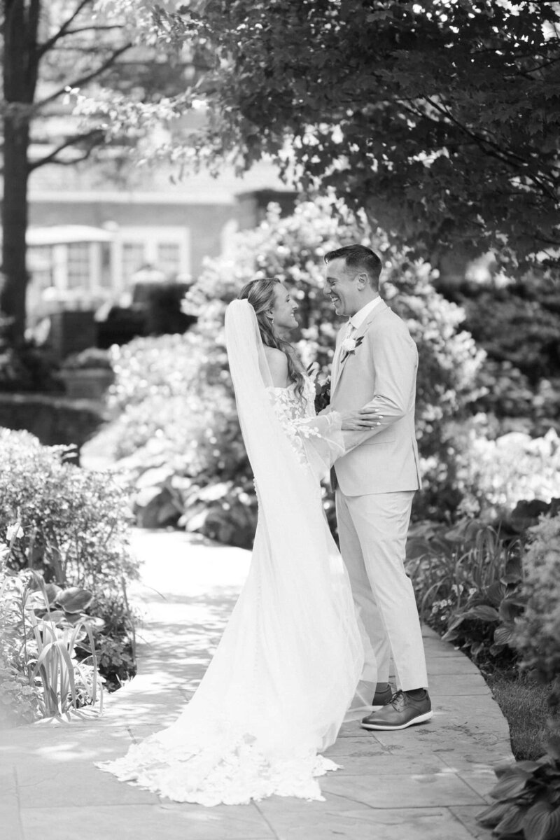 Photo of a bride and groom holding one another, laughing on the lawn of Congress Hall with the hydrangeas in bloom on the background