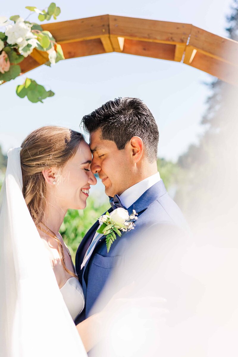 Couple forehead to forehead while brides veil sweeps across entire image