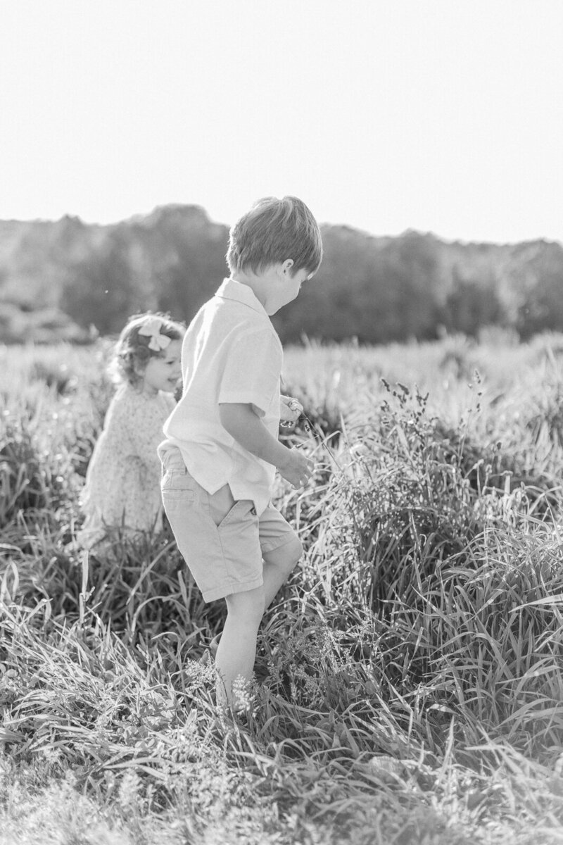 A black and white photo of a little boy and his sister walking through a field at Callahan State Park during photo session with Boston photographer Corinne Isabelle
