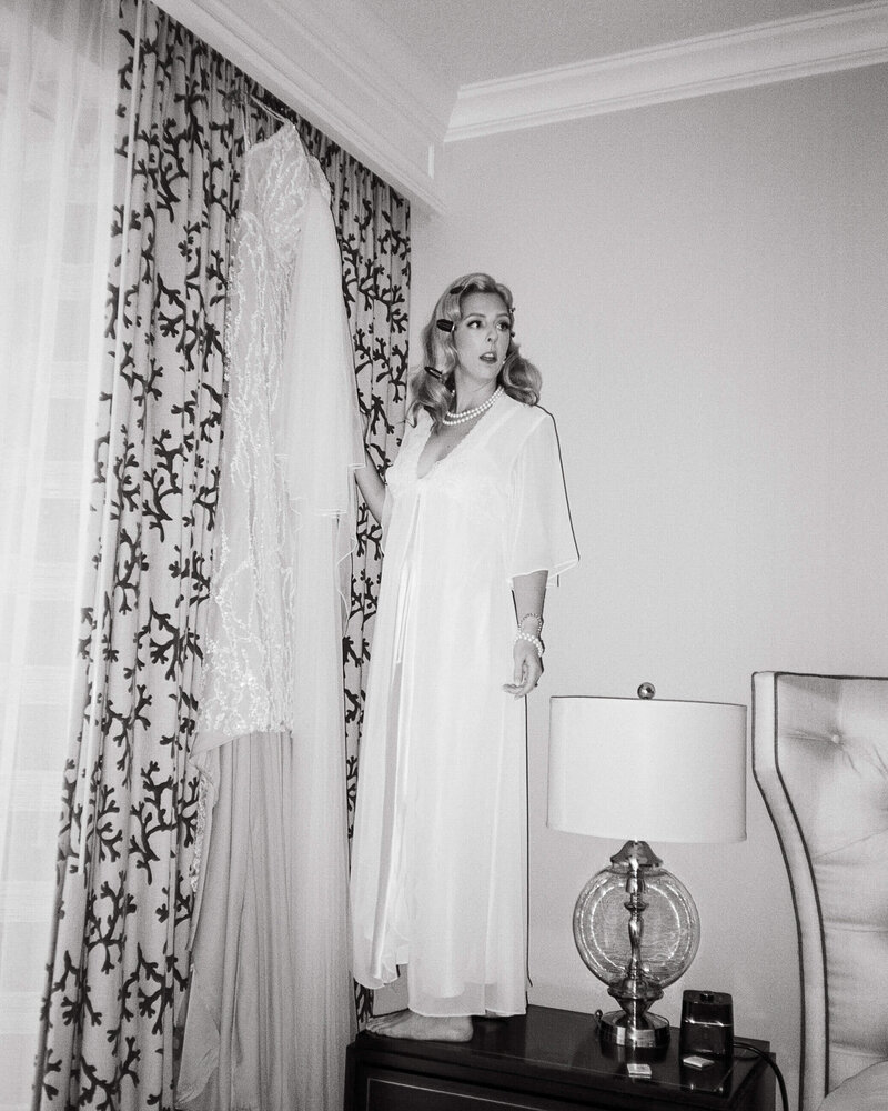 Bride stands on nightstand to retrieve her wedding gown